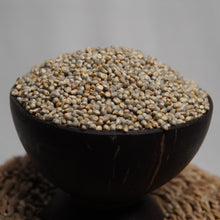 Load image into Gallery viewer, A close-up of Pearl millet piled in a dark bowl, with more of the same scattered around the base against a soft gray background.
